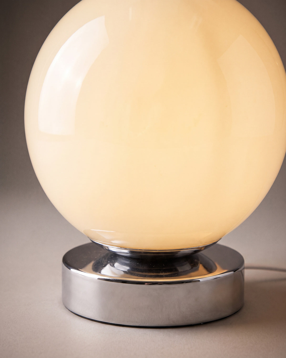 Lampe de table Pleine Lune: gros plan sur la surface brillante de la boule en verre crème et son socle chromé