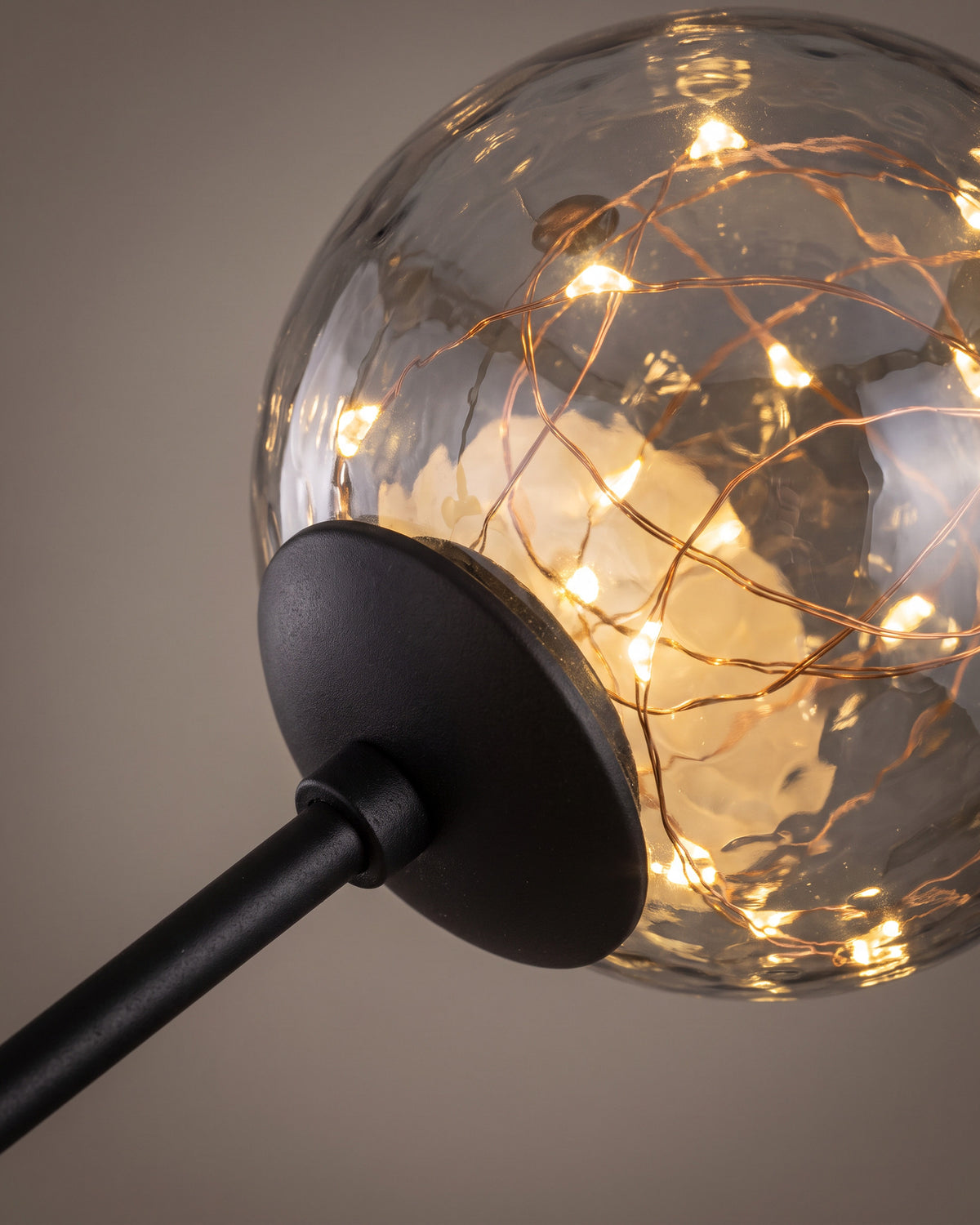 Lustre Pléiade: gros plan sur un globe en verre avec ses guirlandes lumineuses et le bout de bras qui le tient