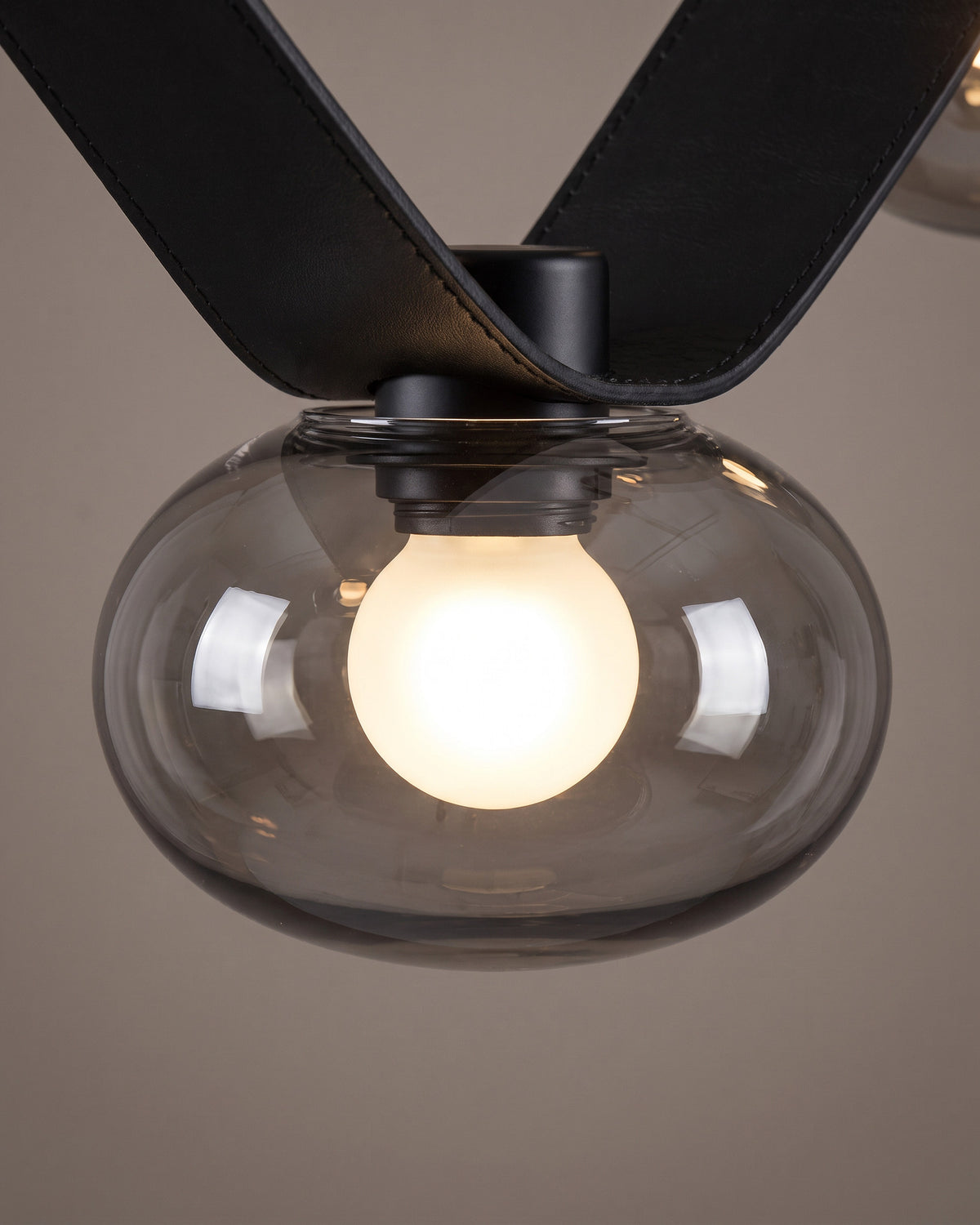Lustre Collier: gros plan sur un globe en verre fumé fixé sur la sangle noire avec son ampoule visible