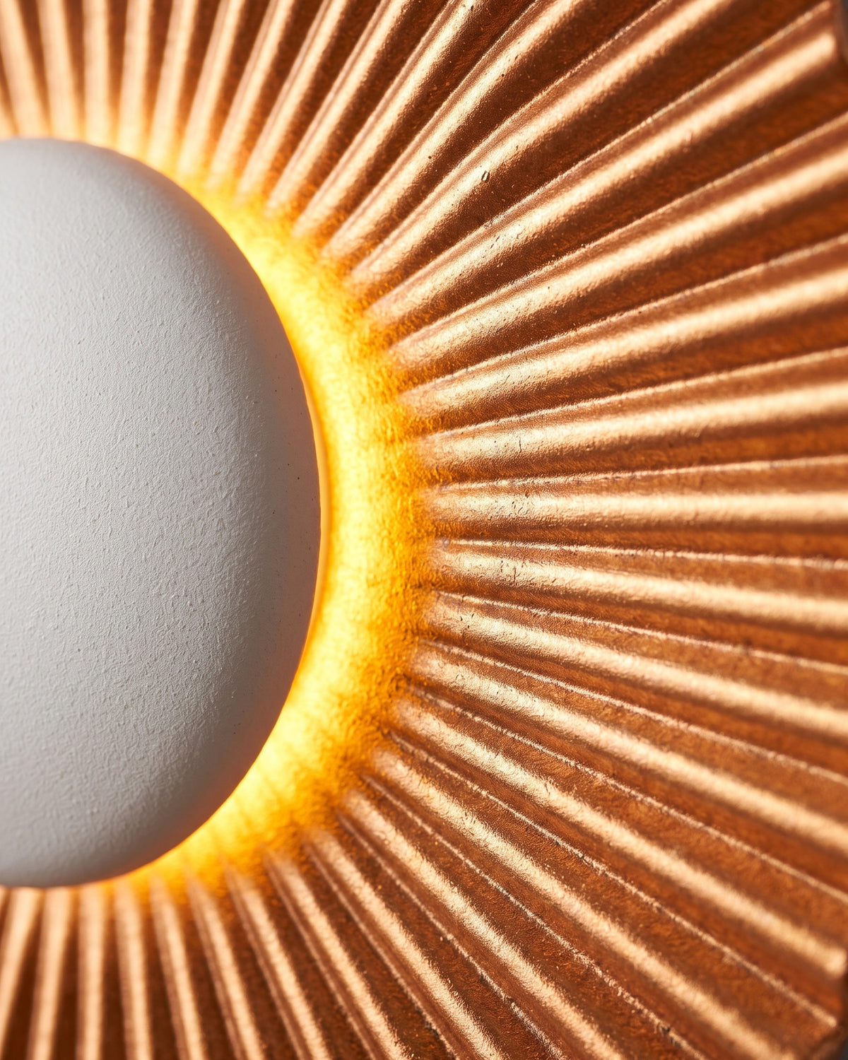 Applique Soleil: gros plan sur les plis rayonnants cuivrés autour du dôme central blanc lumineux