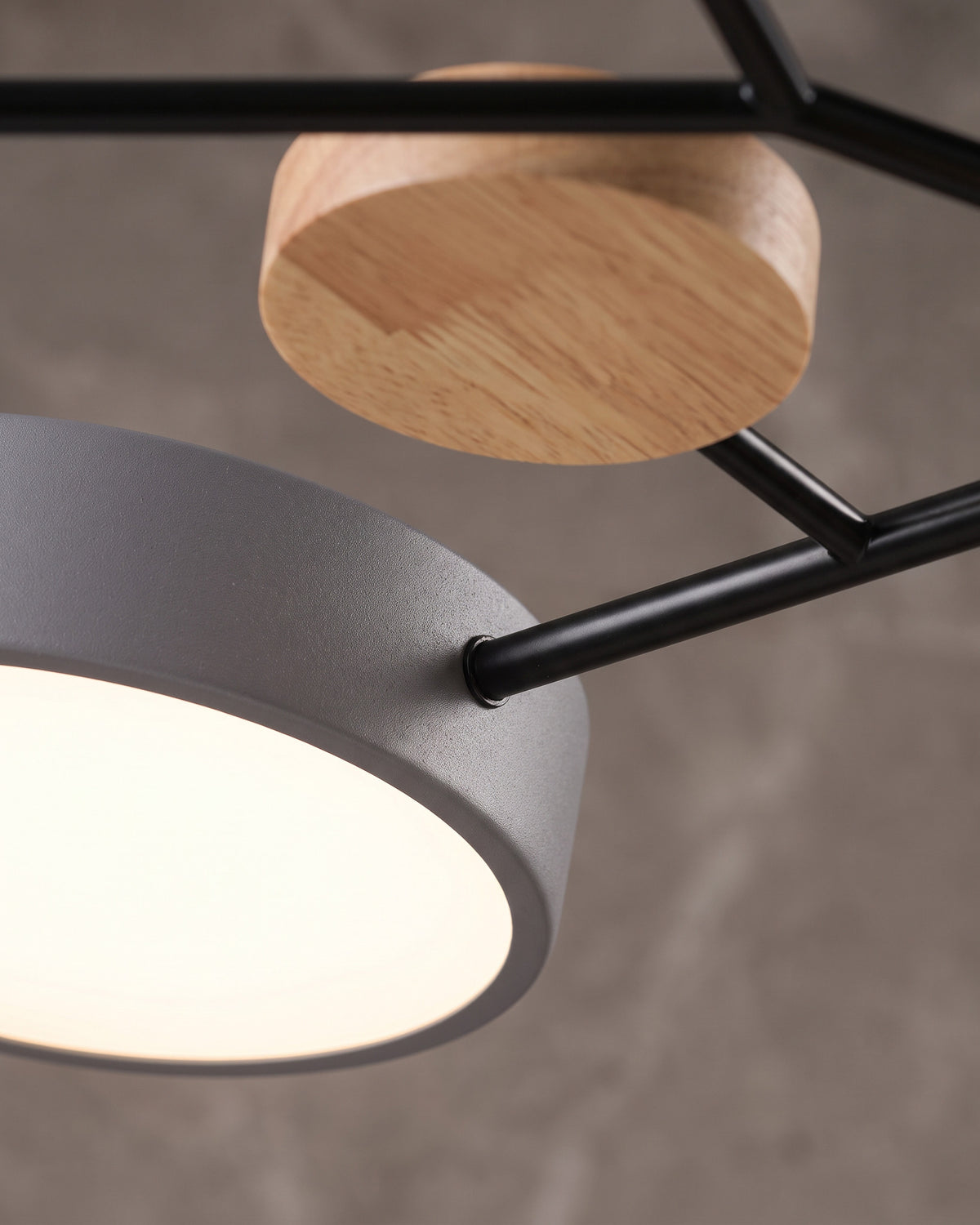 Plafonnier Astre : gros plan sur un disque gris lumineux, un bras noir et une pastille de bois clair