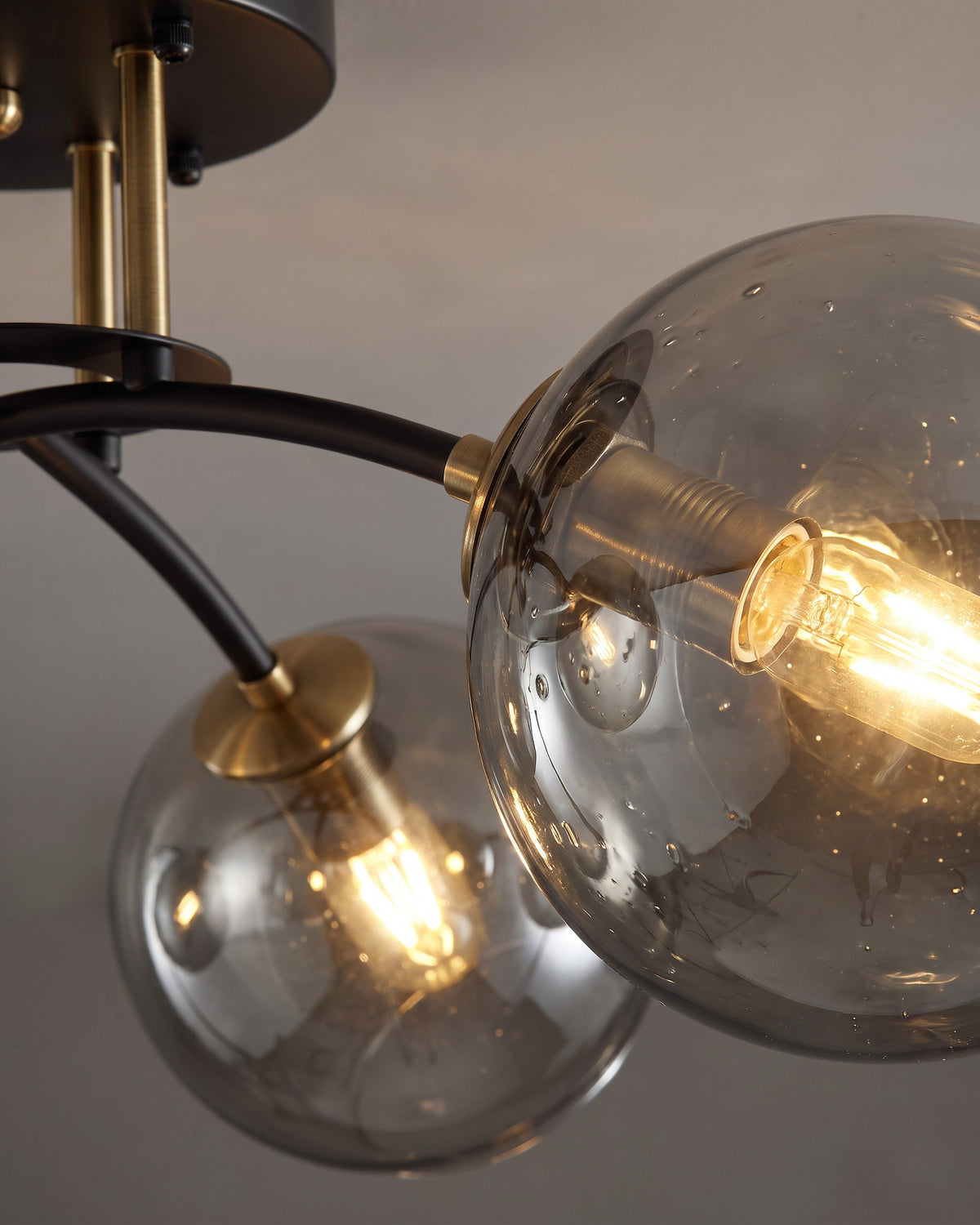 Plafonnier Bulles : gros plan sur deux globes en verre fumé avec la source visible au travers et le bras noir qui les porte
