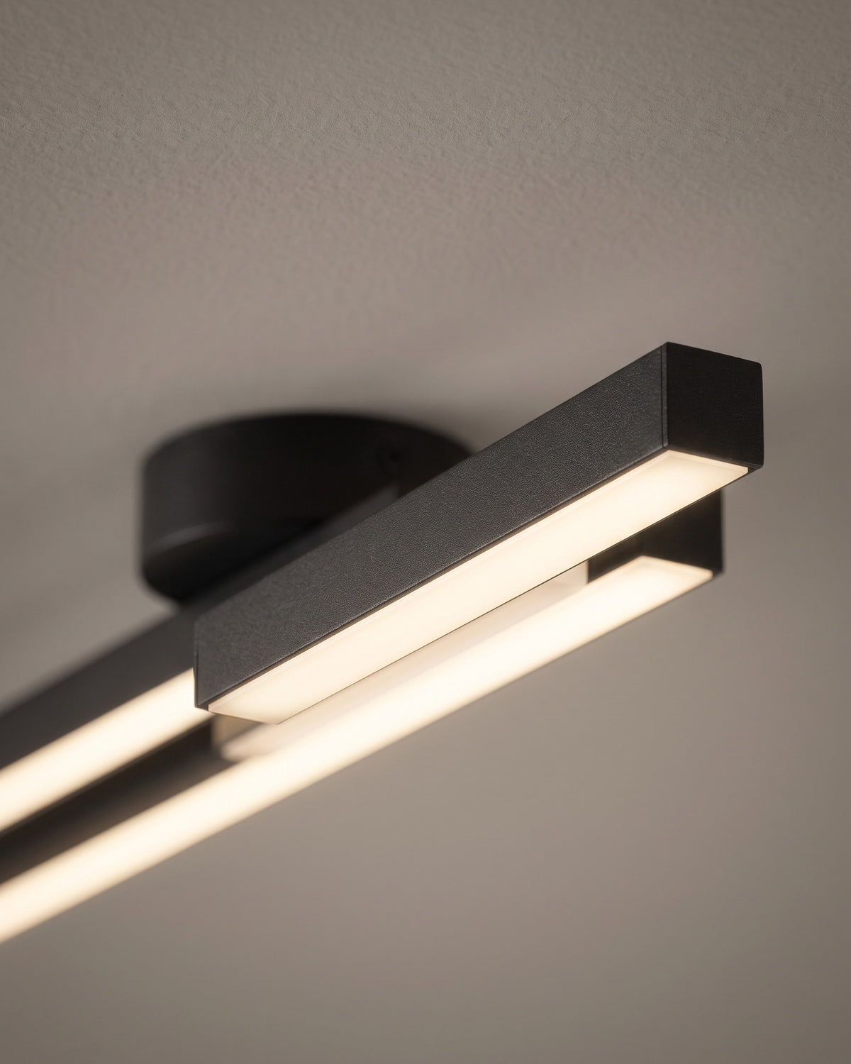 Plafonnier Jumelles: gros plan sur la platine ronde noire et le décalage des deux barres avec leur ligne lumineuse