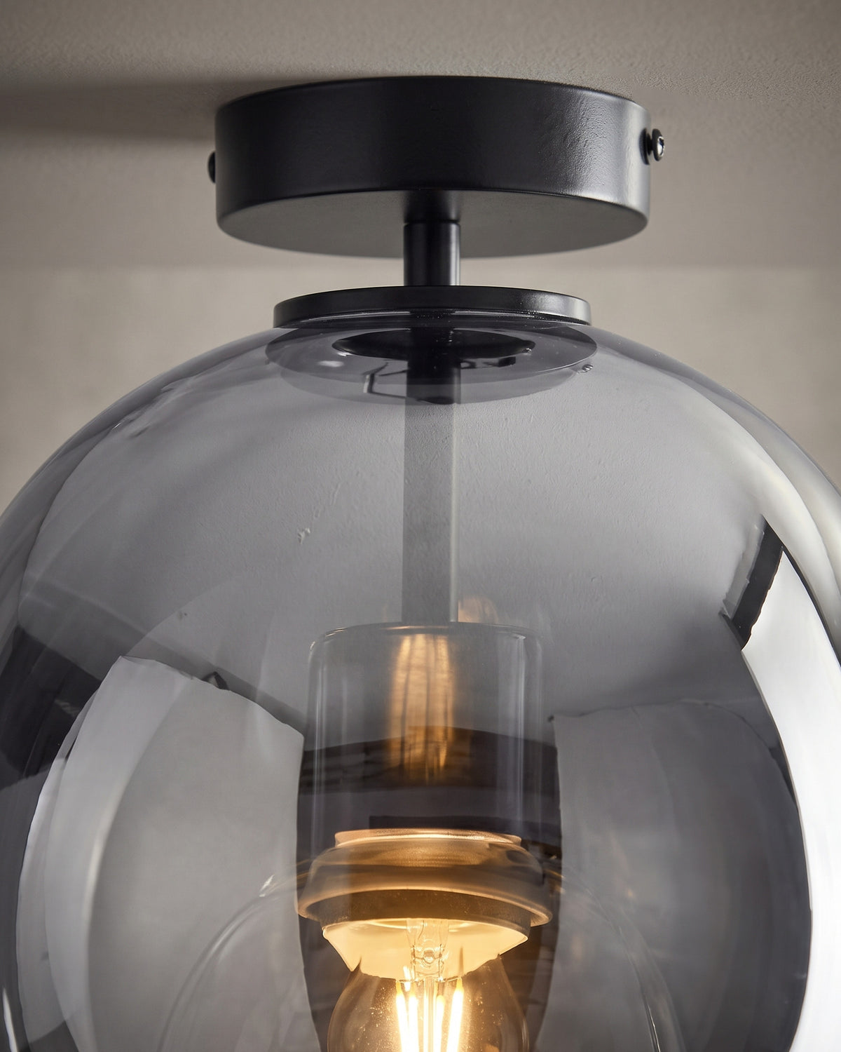 Suspension Fumerolle: gros plan sur la douille noire cerclée de laiton vue à travers le verre fumé