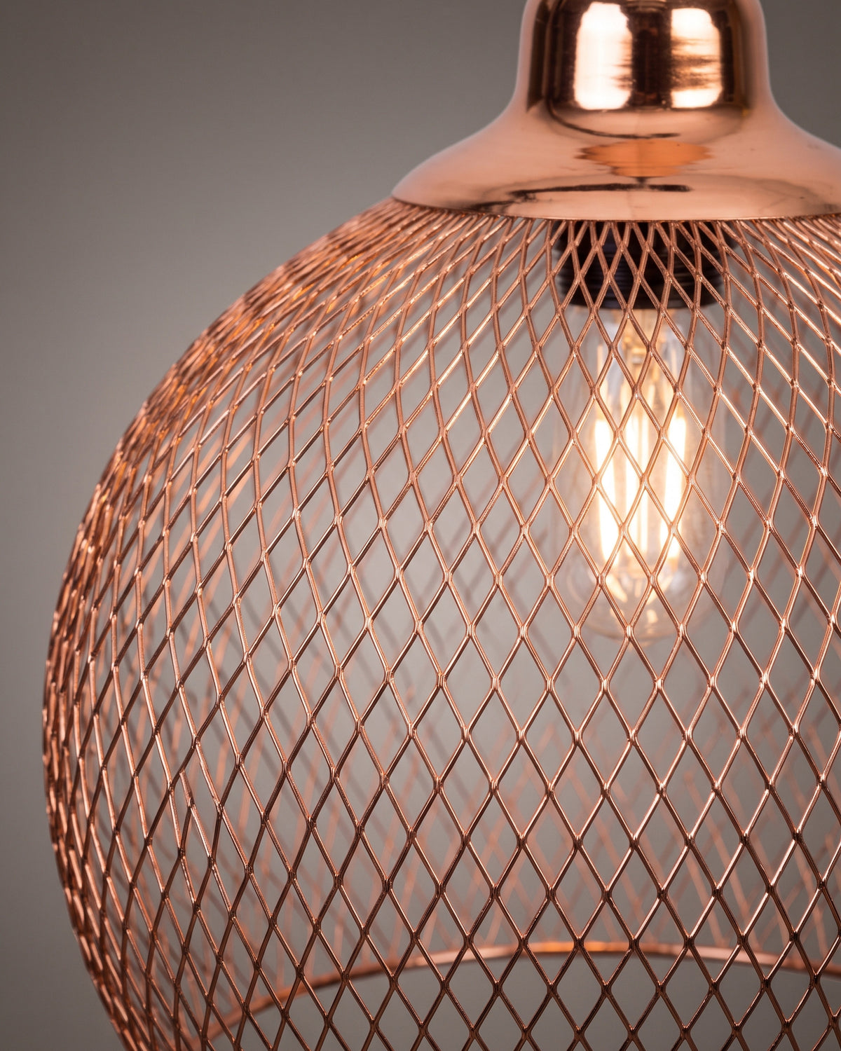 Suspension Résille: gros plan sur le maillage en losanges de la cage et la douille cuivrée avec l'ampoule filament visible au travers