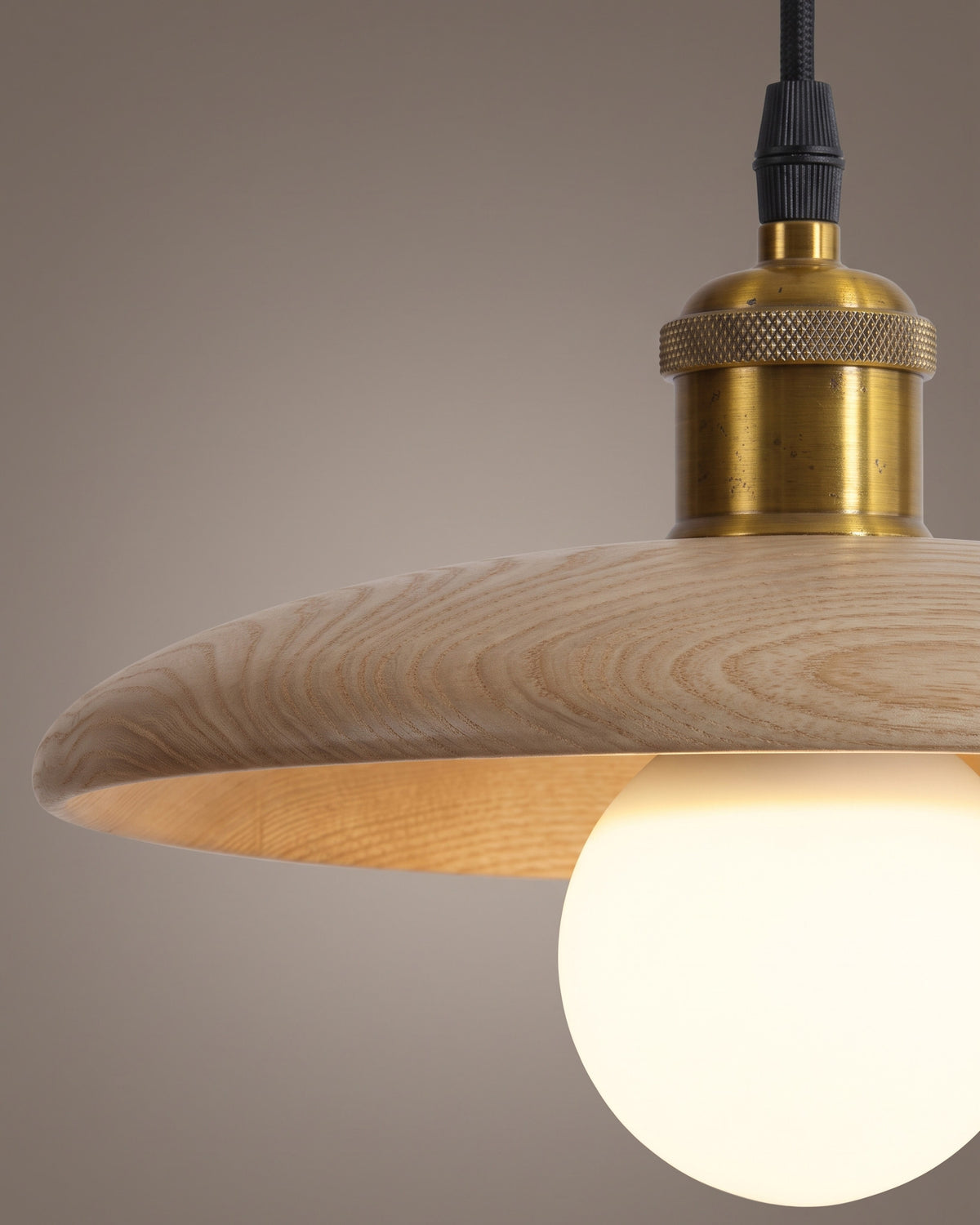 Suspension Béret: gros plan sur la douille dorée posée sur le disque d'aspect bois et l'ampoule globe
