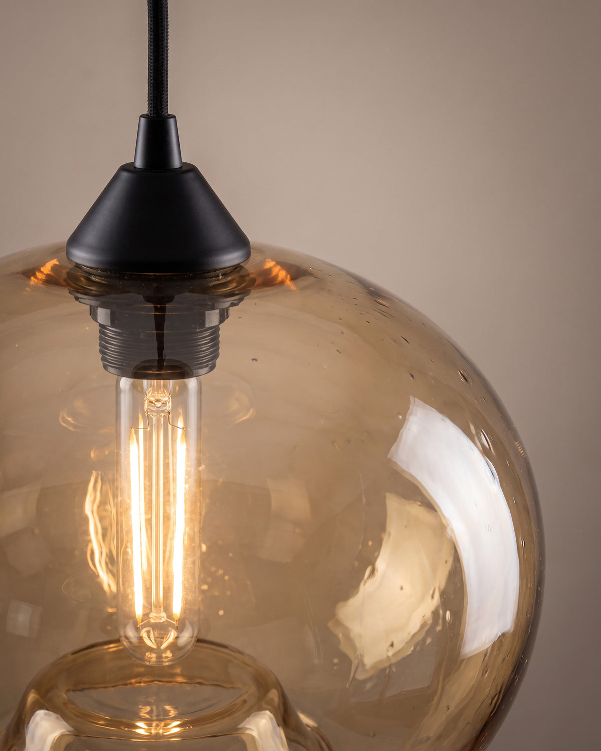 Suspension Larme: gros plan sur la courbe du verre soufflé et l'ampoule à filament sous la douille noire