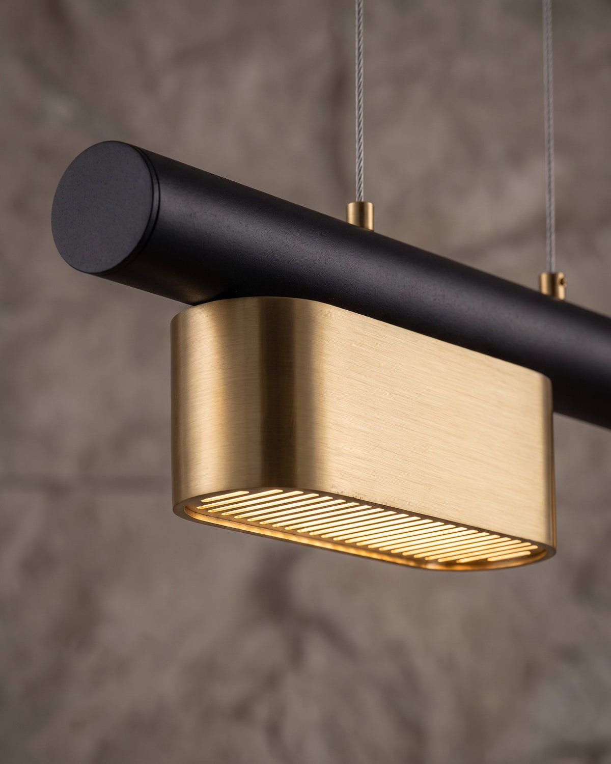 Suspension Pavé : gros plan sur un pavé doré brossé et sa grille lumineuse sous le tube noir